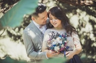 An elegant prewedding portrait with natural light filtering through tropical leaves.