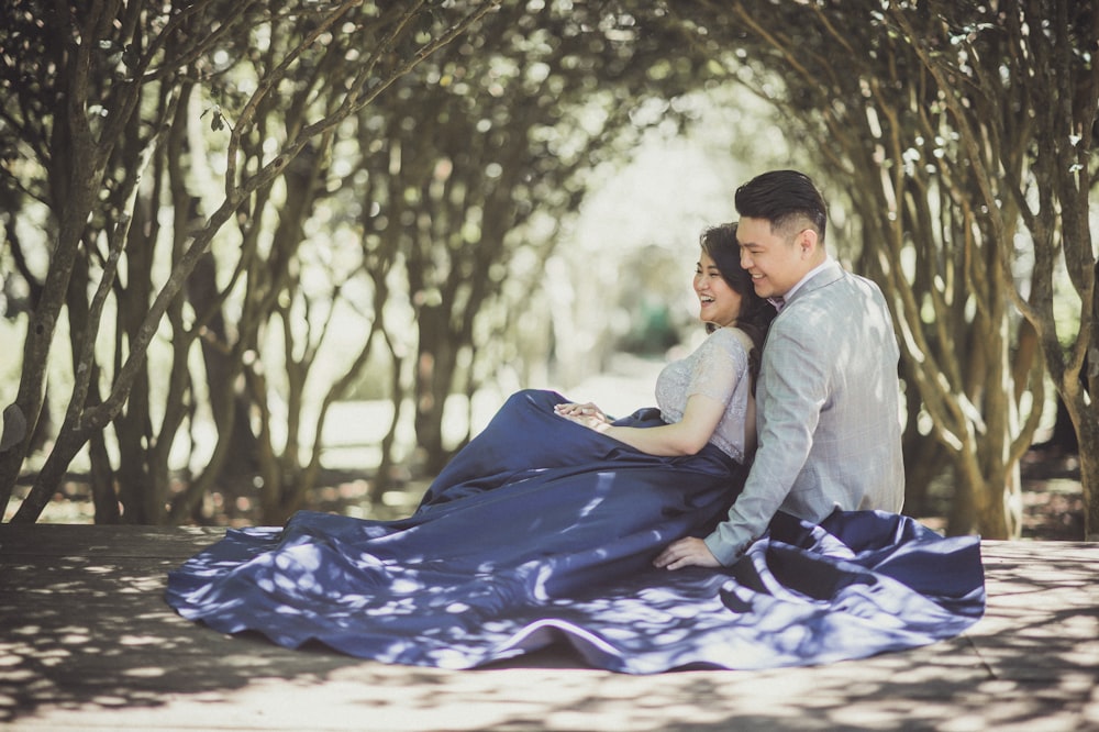 woman leaning with man sitting on ground with blanket under trees during daytime