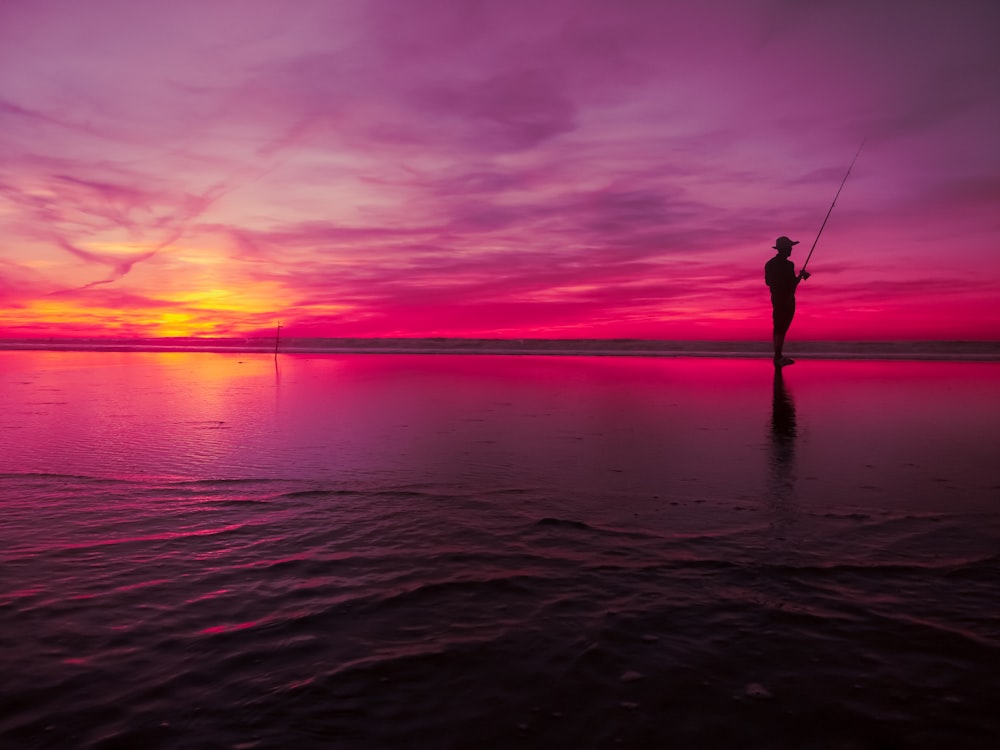 ゴールデンアワーに釣りをしている人のシルエット写真