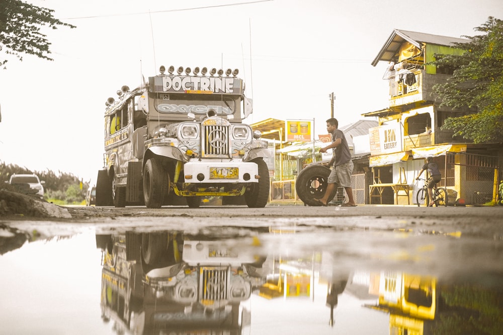 man carrying tire beside gray jeepney outdoors