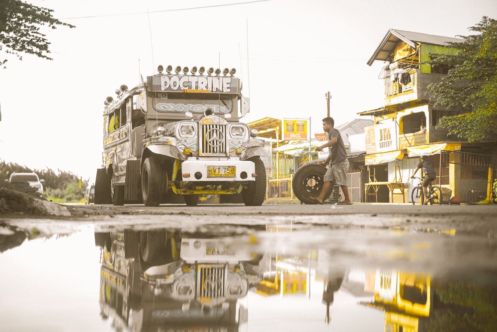 Mann trägt Reifen neben grauem Jeepney im Freien