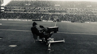 A dynamic black-and-white photo of a football creator filming content on the sidelines of a stadium.