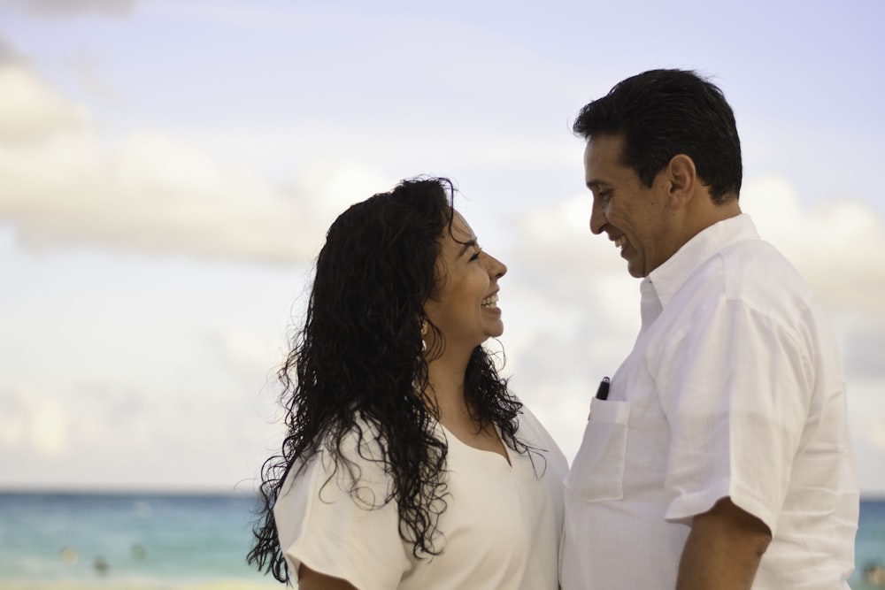 Homem e mulher de frente um para o outro enquanto sorriem na praia