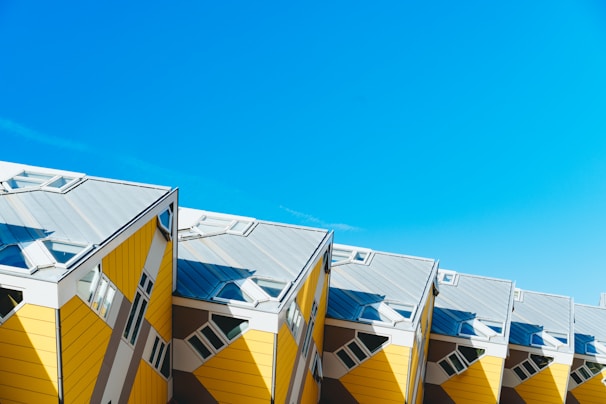 Unique cube-shaped buildings with slanted roofs in bright yellow contrast against a clear blue sky, showcasing modern architectural design.