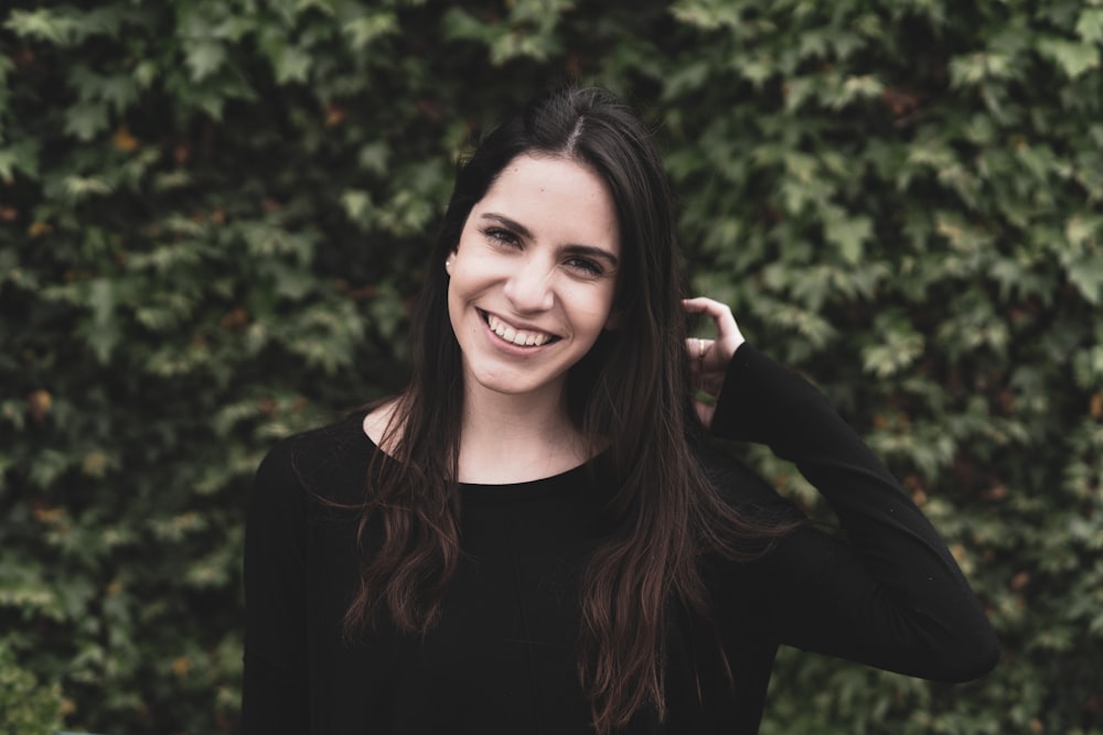 a smiling woman in a black top stands in front of a bush