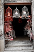 A collection of colorful nets are displayed hanging around an open doorway. The nets have various shapes and contain objects like floats inside them, creating an interesting pattern. The entrance is framed by rough, weathered stone, adding a rustic charm.