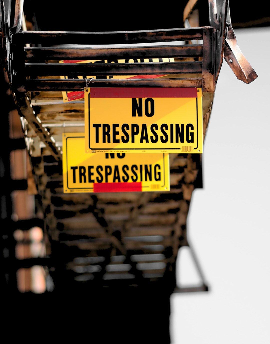 These NO TRESPASSING signs are hanging from a fire escape on a downtown building.