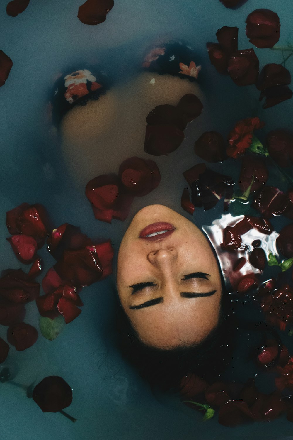 赤い花びらで満たされた水に浸かり、水面に顔を出す女性