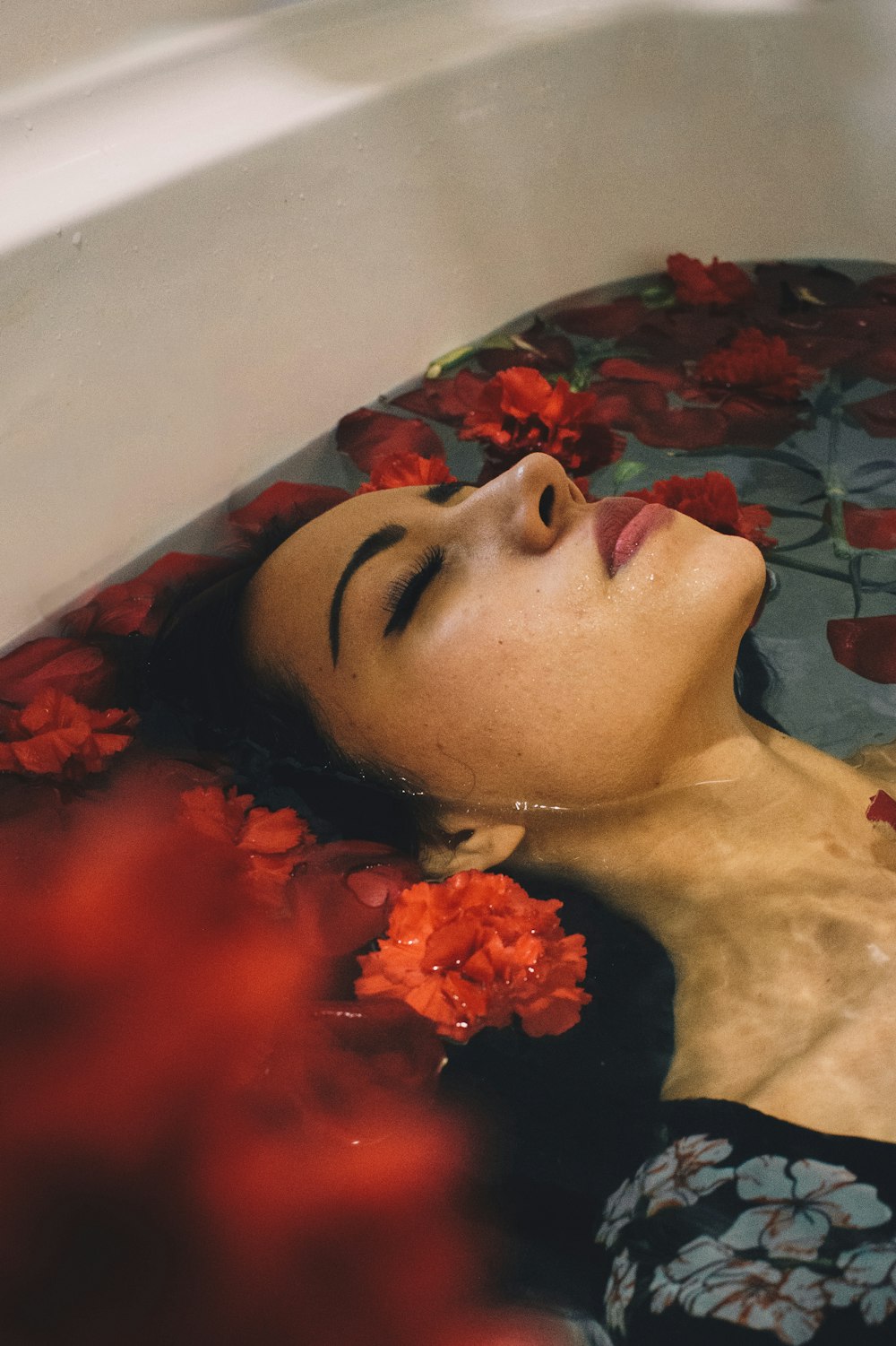 woman in grey and black floral dress submerge into bathtub with red flowers