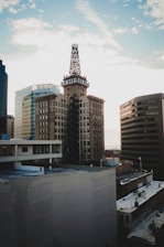 A cityscape featuring a prominent historic building with a rooftop sign that reads 'CENTER CENTER'. The scene includes modern office buildings, and the sky is partly cloudy with sunlight illuminating the urban setting.