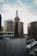 A cityscape featuring a prominent historic building with a rooftop sign that reads 'CENTER CENTER'. The scene includes modern office buildings, and the sky is partly cloudy with sunlight illuminating the urban setting.