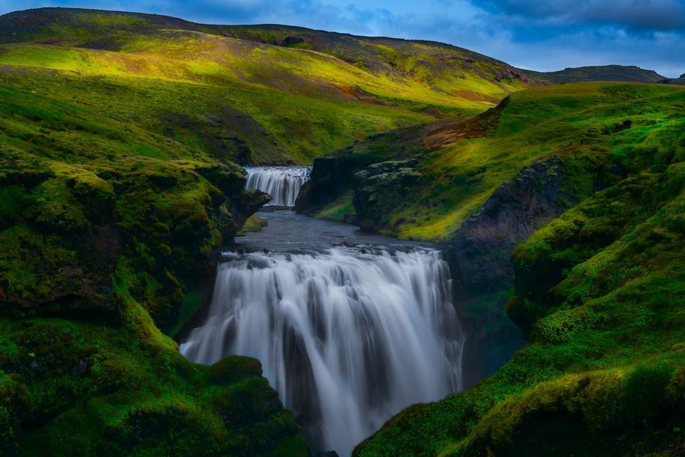 waterfalls between grass-covered hills during daytime
