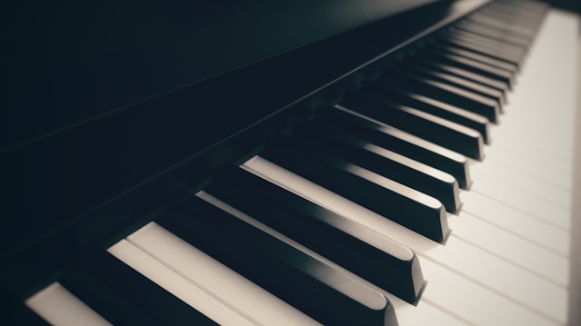A close-up view of piano keys, showing a perspective that highlights the alternating pattern of black and white keys. The image has a soft focus and warm lighting, creating a classic and elegant ambiance.