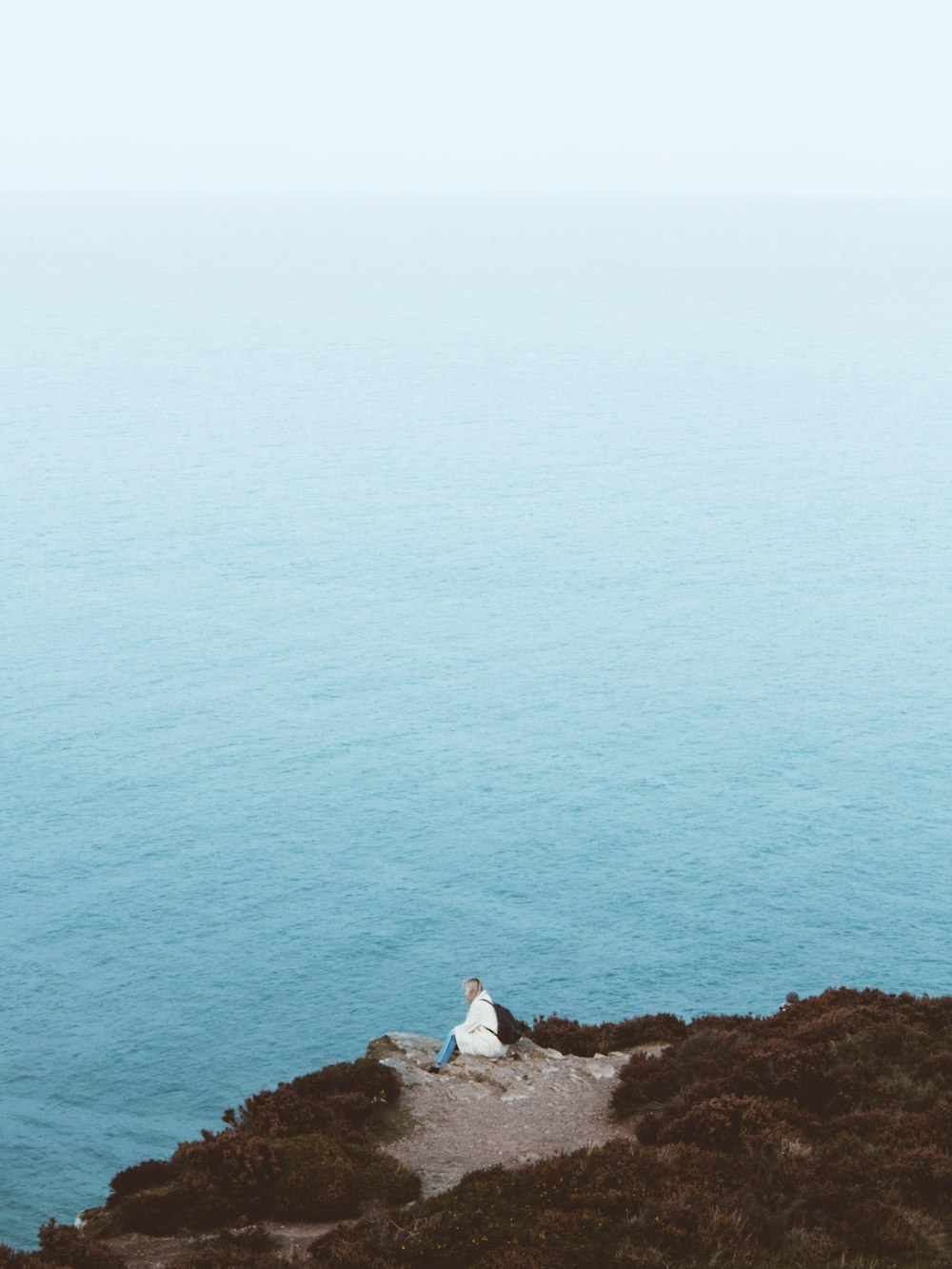 person sitting on cliff overlooking sea