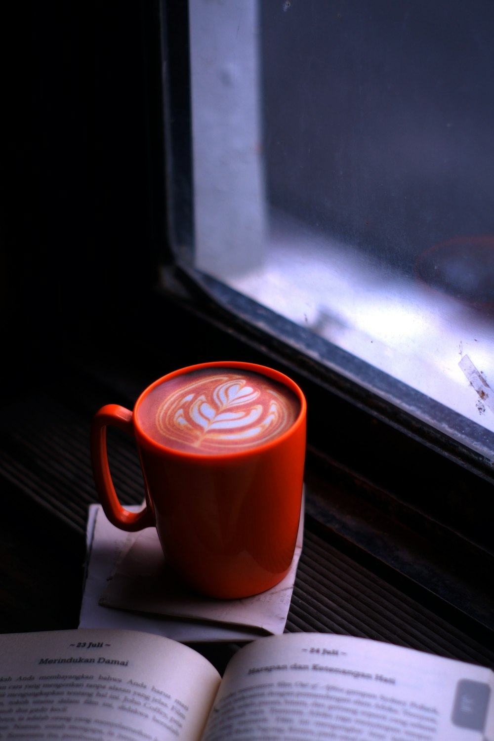 red ceramic mug with coffee beside white book