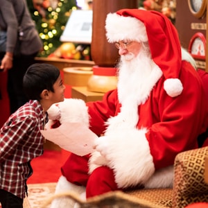 boy standing in front of man wearing Santa Claus costume