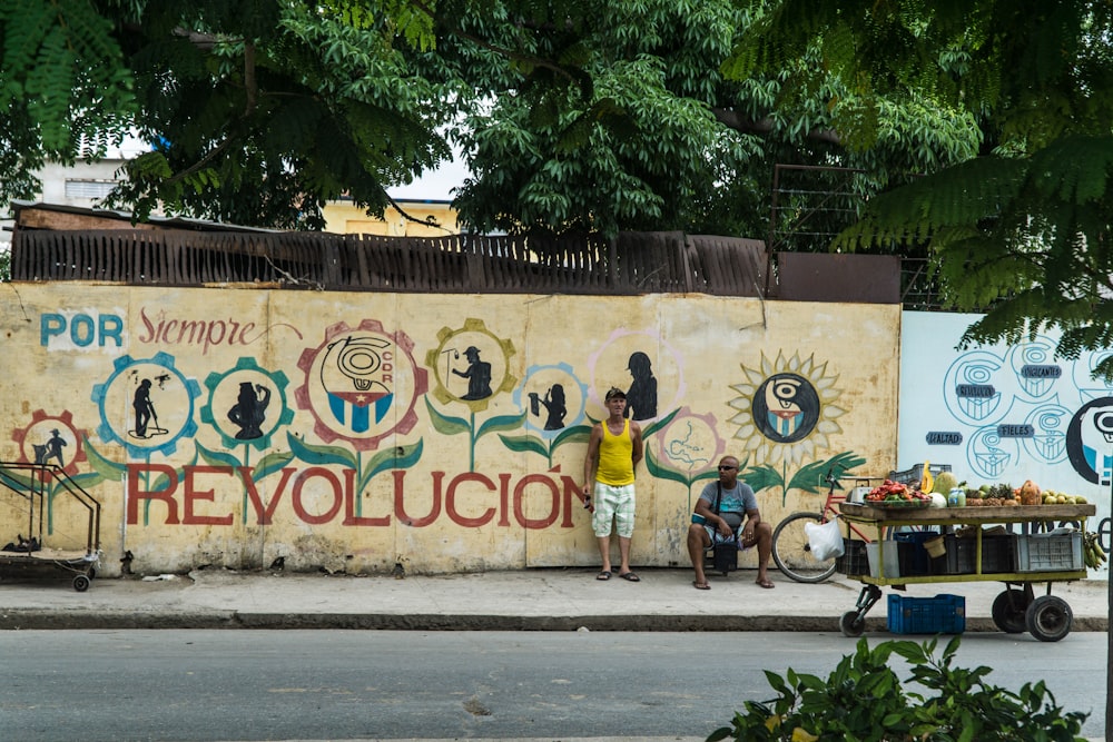 dois homens em pé perto da parede com mural