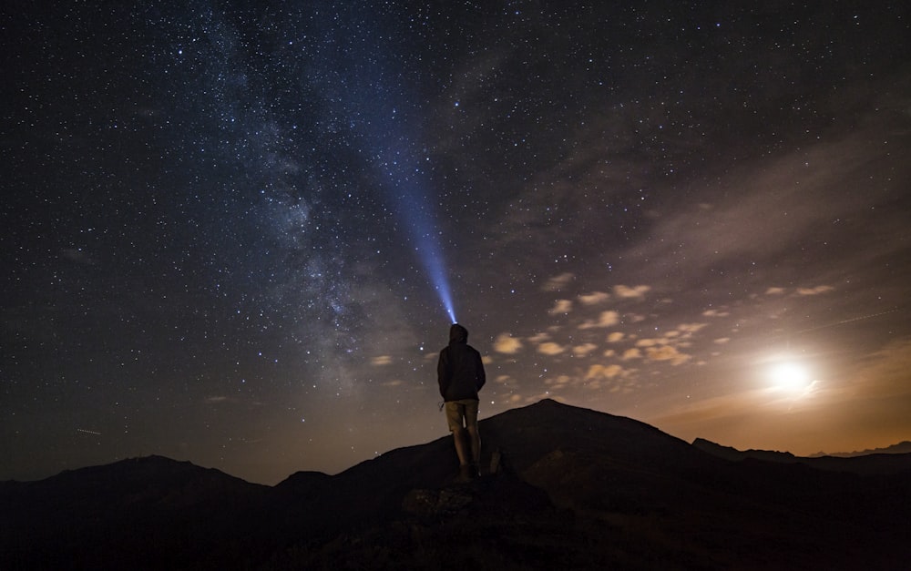 Homem em pé no pico da montanha sob o céu noturno estrelado