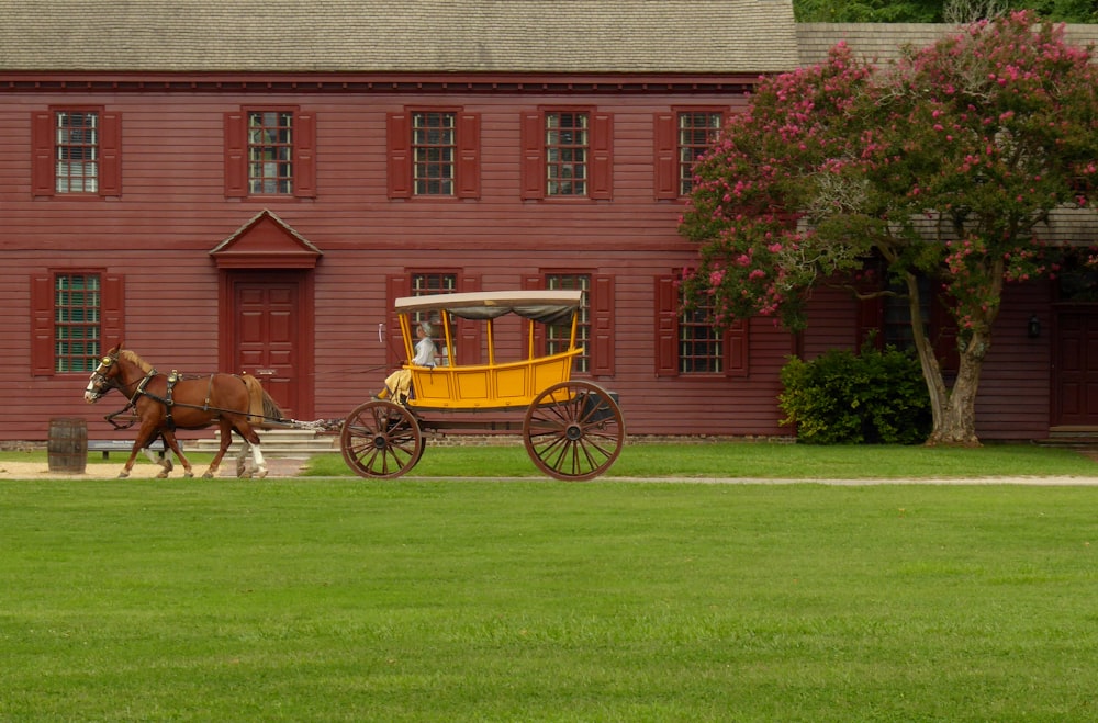 赤いコンクリートの家の横に黄色い馬車を載せた茶色の馬