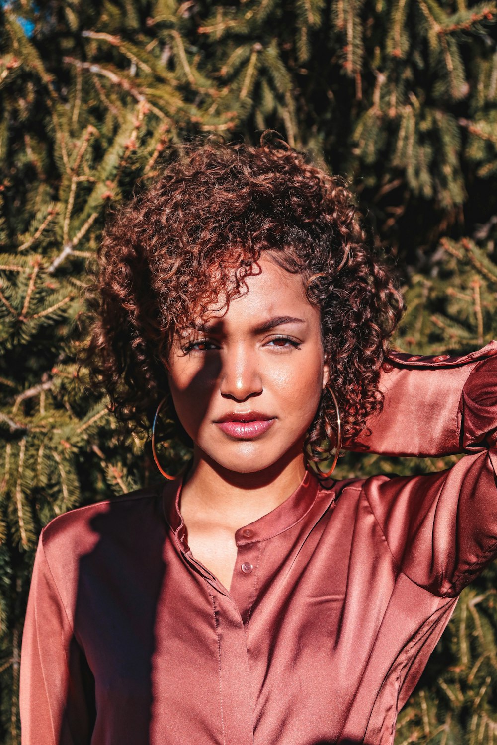 woman wearing red button-up long-sleeved shirt under shade of hand near tree at daytime