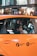 A young person sits inside an orange taxi, looking out the window. The view includes the side of the taxi with metered fare and flat fare JFK markings. The background shows a blurred cityscape with lights and indications of movement.