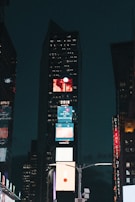 A nighttime cityscape of New York with theater marquees glowing alongside digital billboards promoting AI in film.