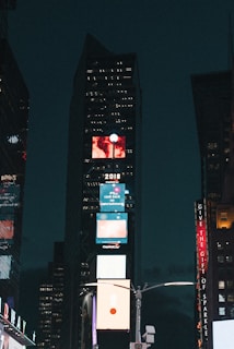 A nighttime cityscape of New York with theater marquees glowing alongside digital billboards promoting AI in film.