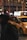A yellow taxi is parked on a dimly lit city street, with bright advertisements on its rooftop. The background shows a bustling urban environment with neon signs and a blurred pedestrian passing by.