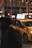 A yellow taxi is parked on a dimly lit city street, with bright advertisements on its rooftop. The background shows a bustling urban environment with neon signs and a blurred pedestrian passing by.