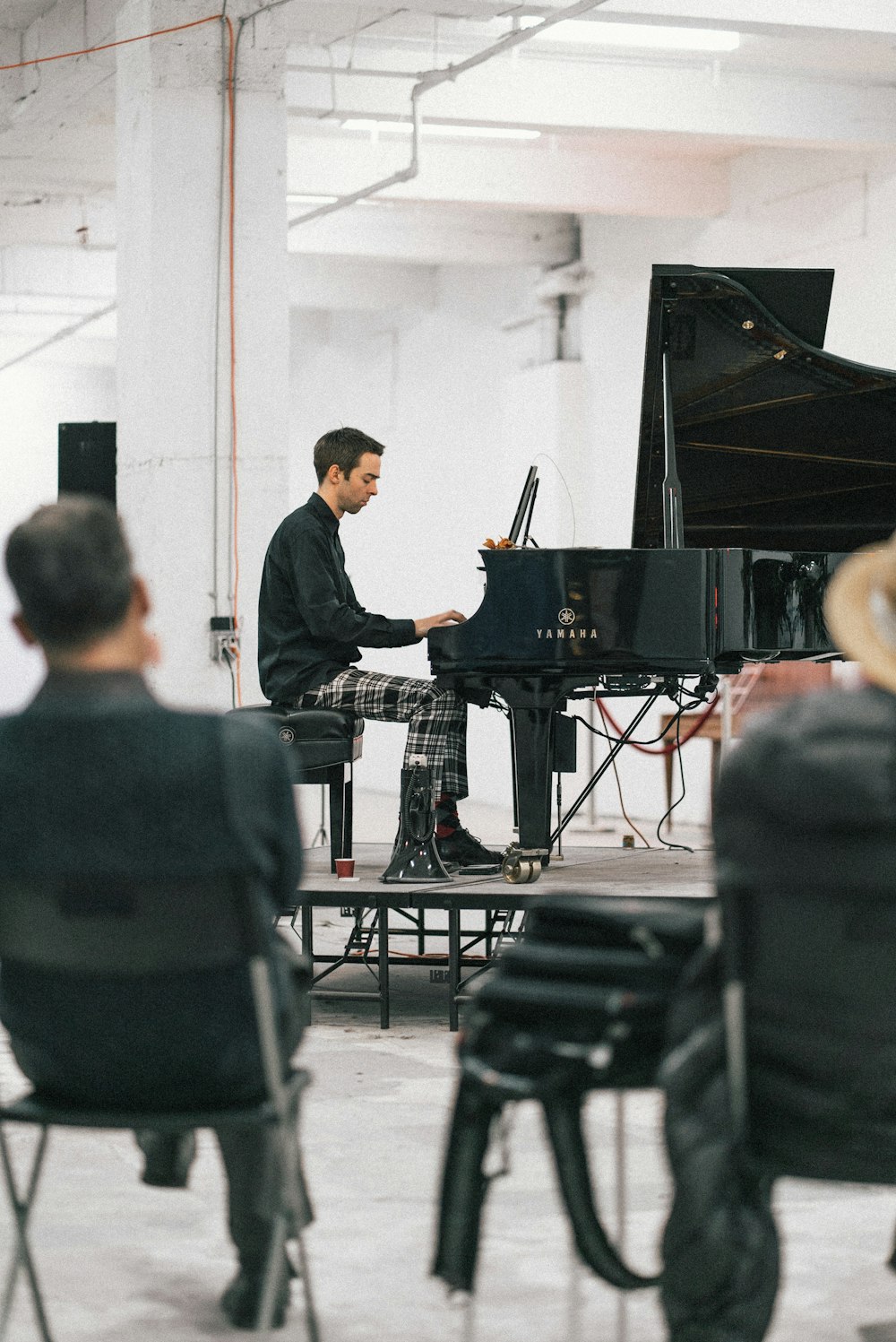 man playing piano on top of stage near two men sitting on chair inside room