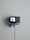 A small television set is mounted on a minimalist white shelf against a plain wall. The screen displays a close-up image of human lips. The setup suggests a blend of vintage and modern aesthetics.