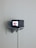 A small television set is mounted on a minimalist white shelf against a plain wall. The screen displays a close-up image of human lips. The setup suggests a blend of vintage and modern aesthetics.