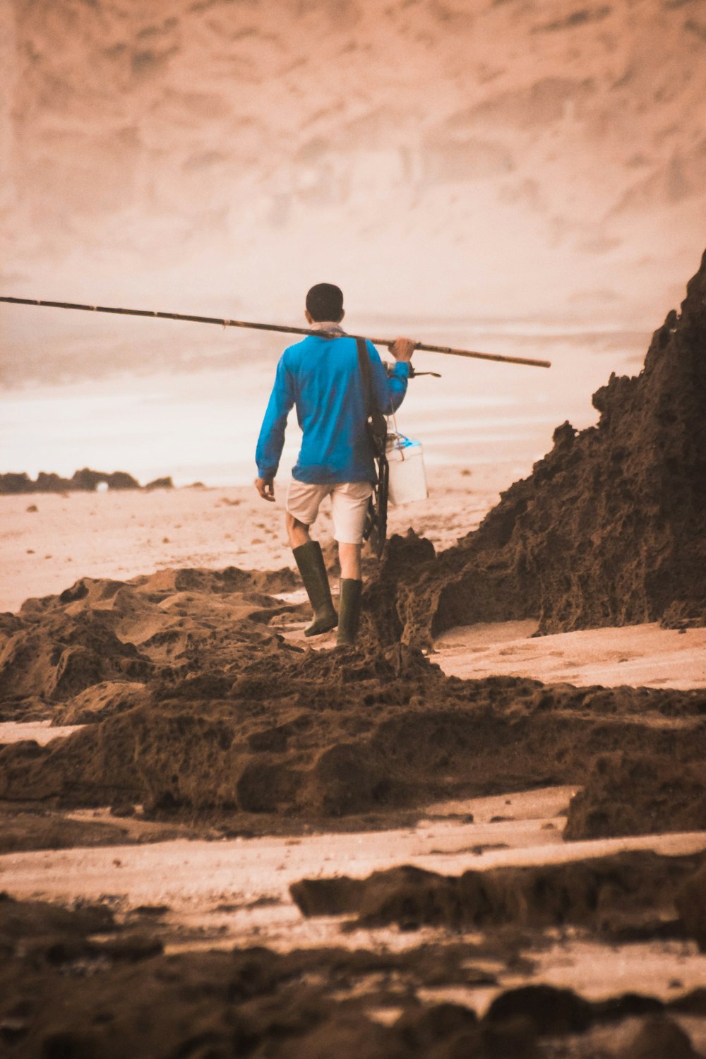 man walking on shore holding rod