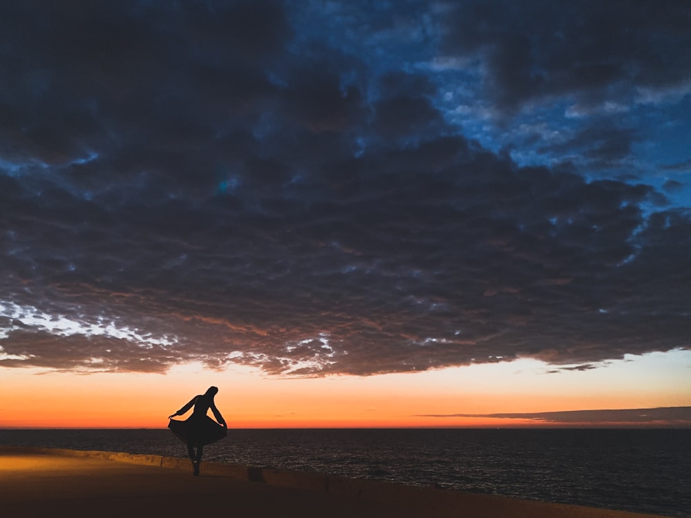 silhouette photography of woman standing near body of water