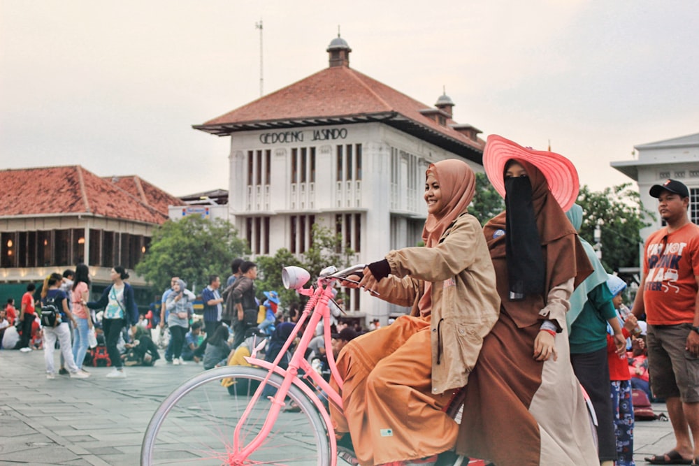 2 woman riding bike beside people by building during daytime