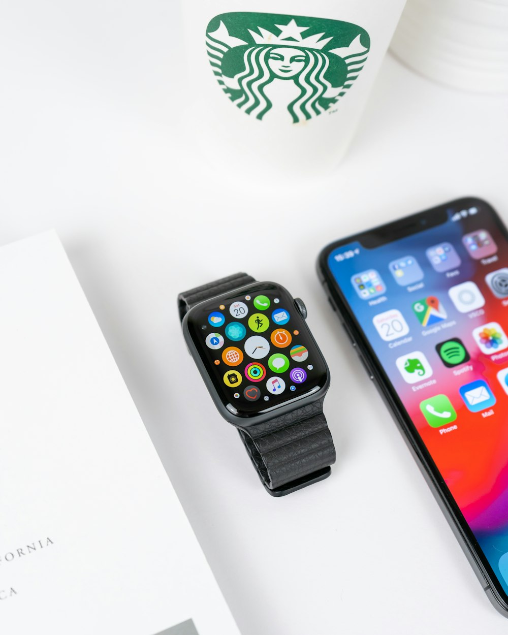 black aluminum case Apple Watch with black Sport Band beside space gray iPhone X turned on