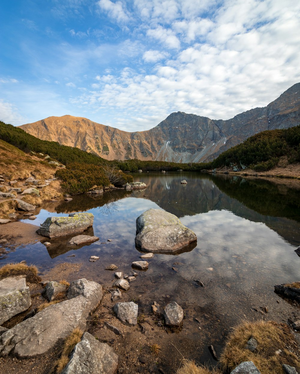 rocks in body of water facing mountain under blue sky