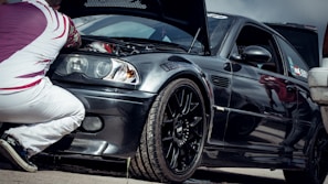 A confident mechanic kneeling beside a car with the hood open on a quiet Florence street