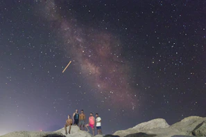 A group of visitors gazing upward, their faces lit gently by starlight in a remote mountain setting