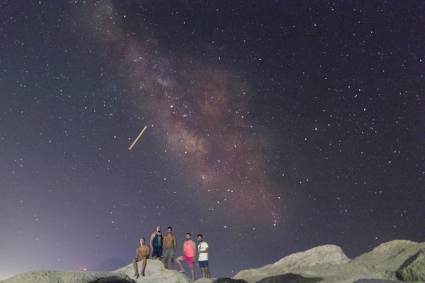 A group of hikers gathered around a guide pointing out constellations in a star-filled night sky.