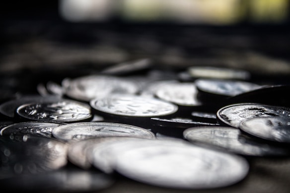 A close-up shot of scattered coins, predominantly silver in color, with a blurred background. The focus is sharp on the front coins, creating a sense of depth.