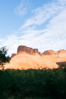 A sunlit mesa towering over a desert landscape with scattered shrubs.
