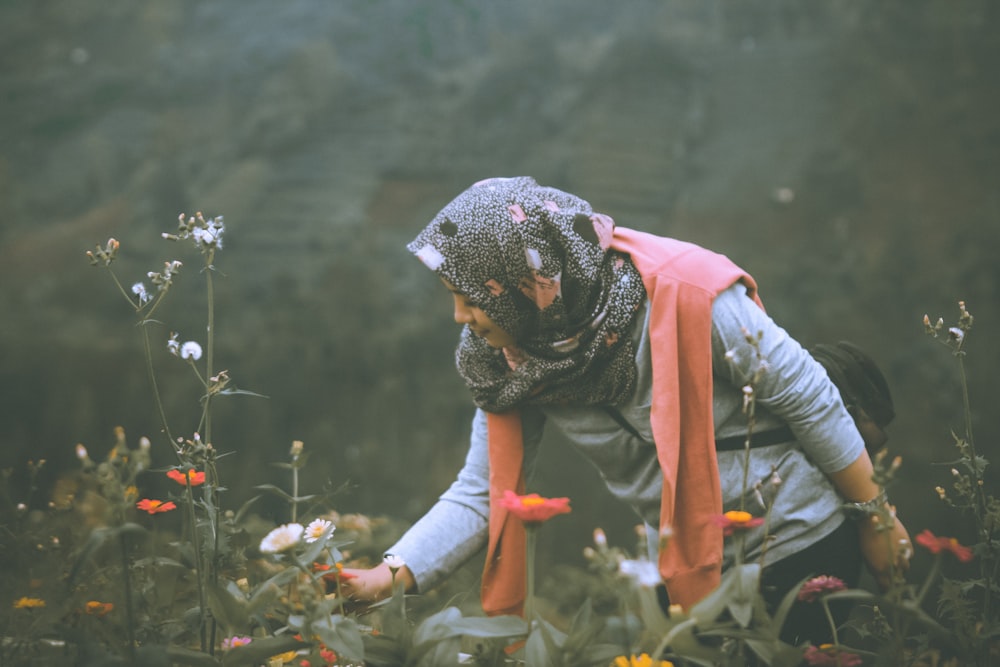 woman in grey and red scarf holding flower in garden