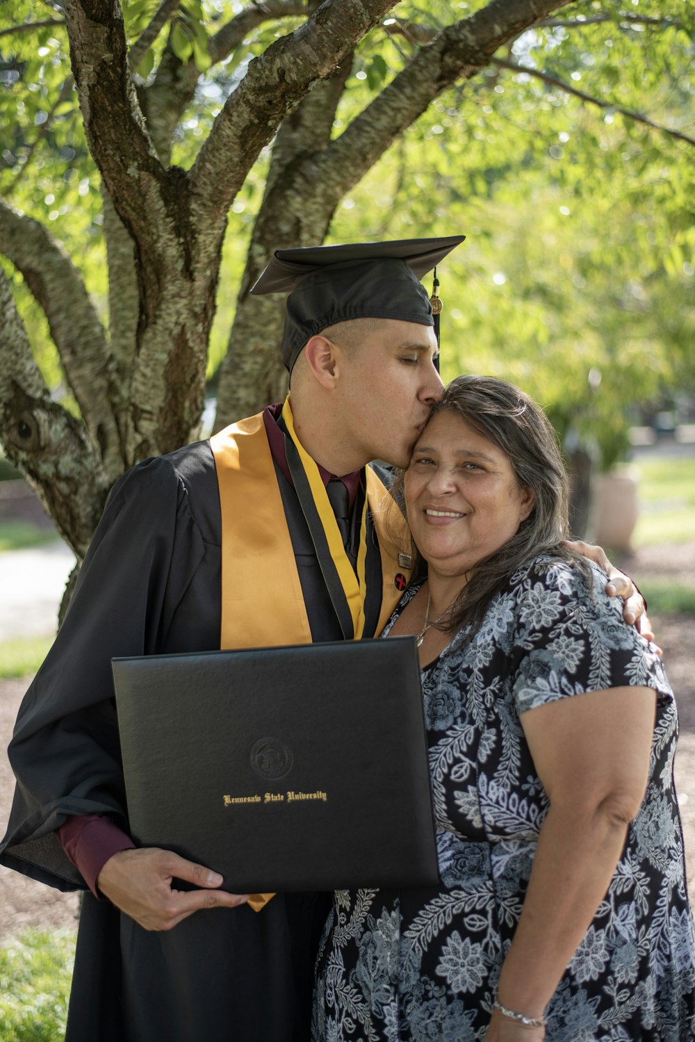 man wearing black graduation gown kissing on woman head