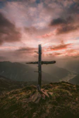 A rustic wooden cross standing on a hill against a dramatic sky at sunset.