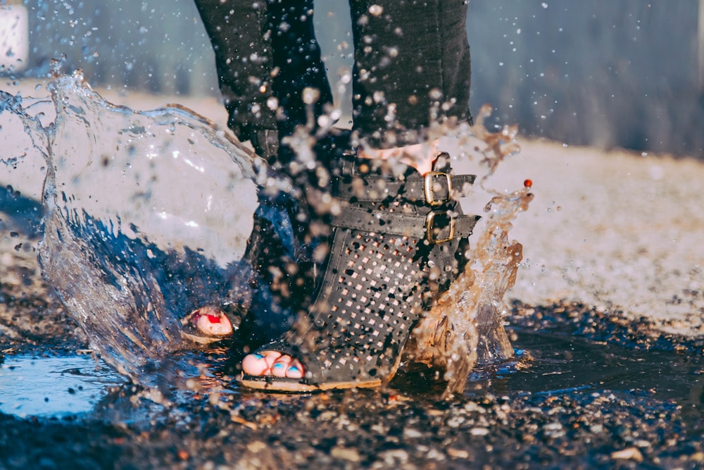 person in black pants and grey mules stepping on puddle