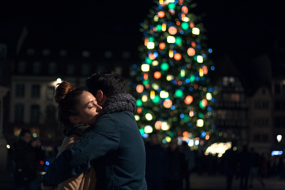 selective focus photography of man and woman hugging each other near Christmas tree