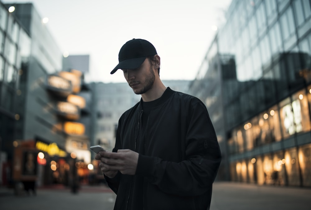 man in black jacket wearing black fitted cap while using phone