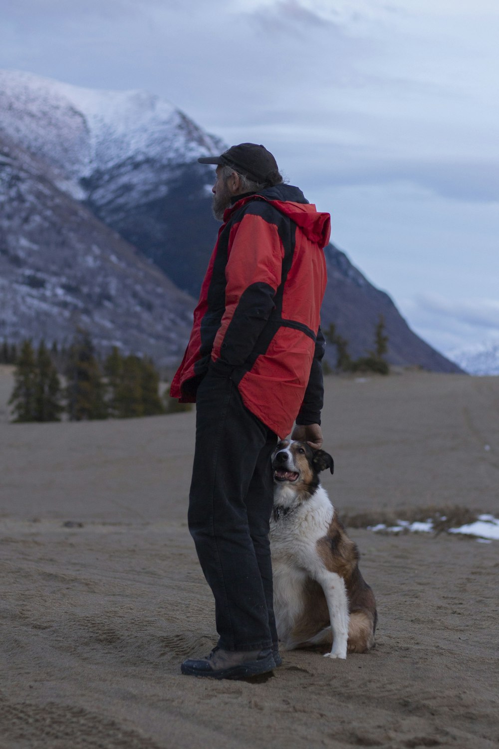 man wearing red jacket standing beside dog