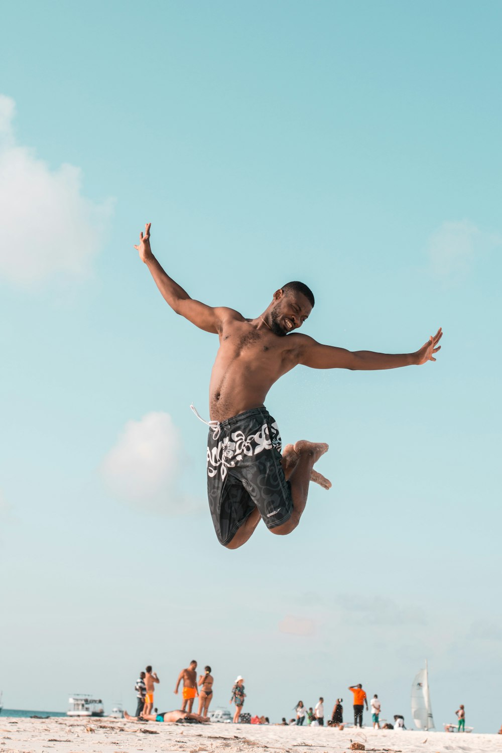 man jumping while spreading his arms and folding his legs at the beach during day